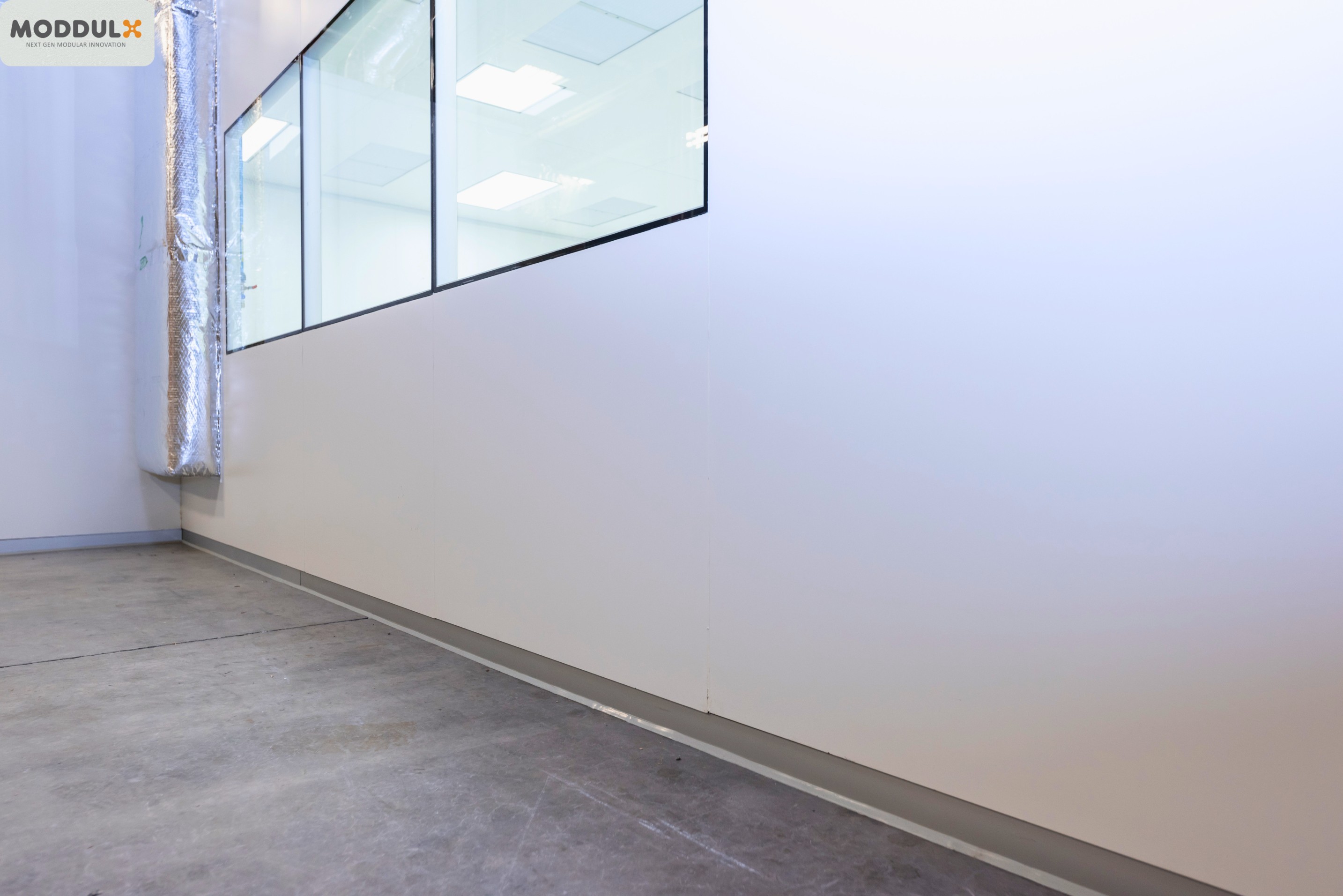 Modular cleanroom wall panel installation with adjustable aluminum base channel and flush floor coving on concrete slab.