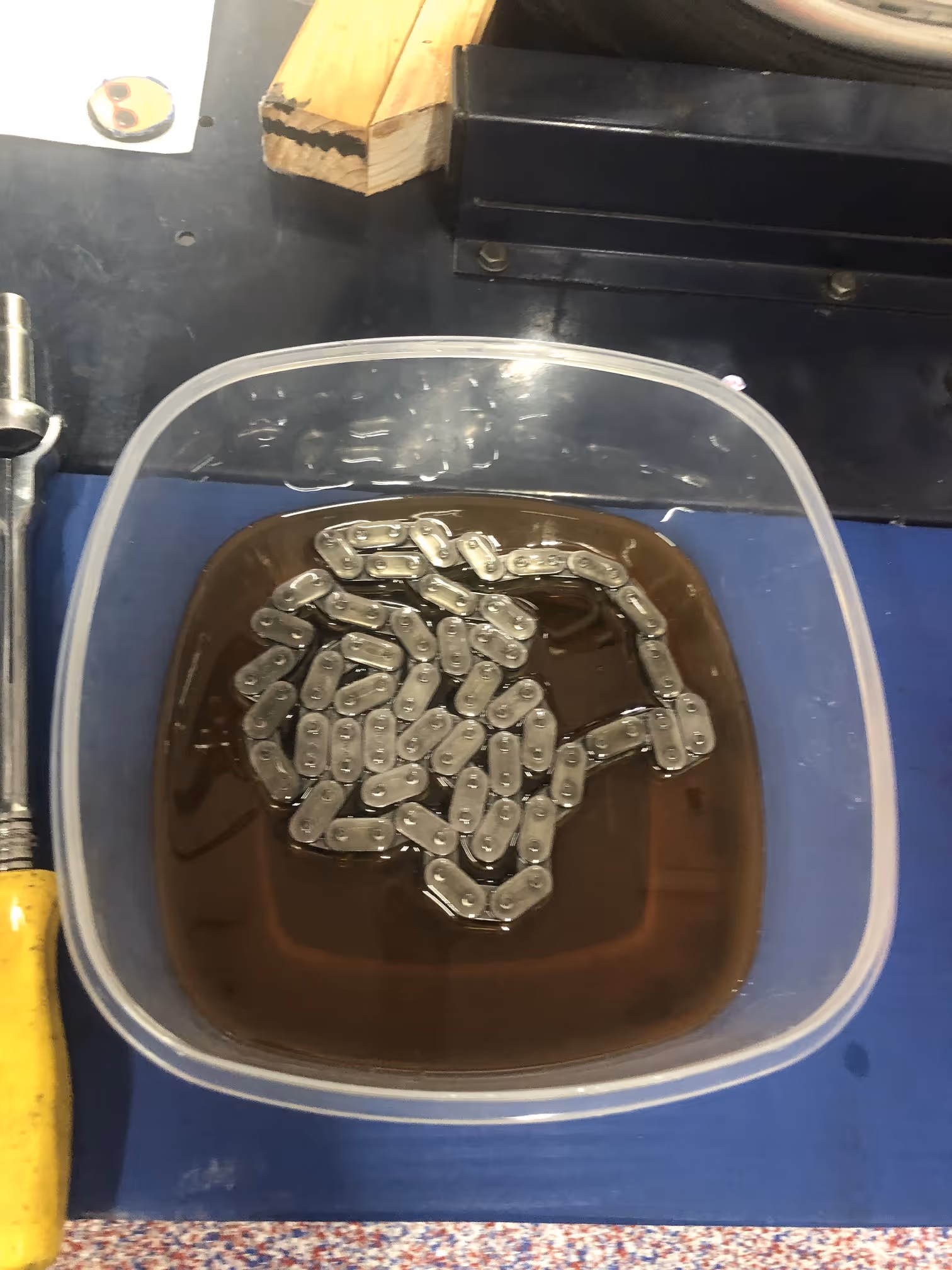Metal chain submerged in a container filled with dark oily liquid on a workbench.