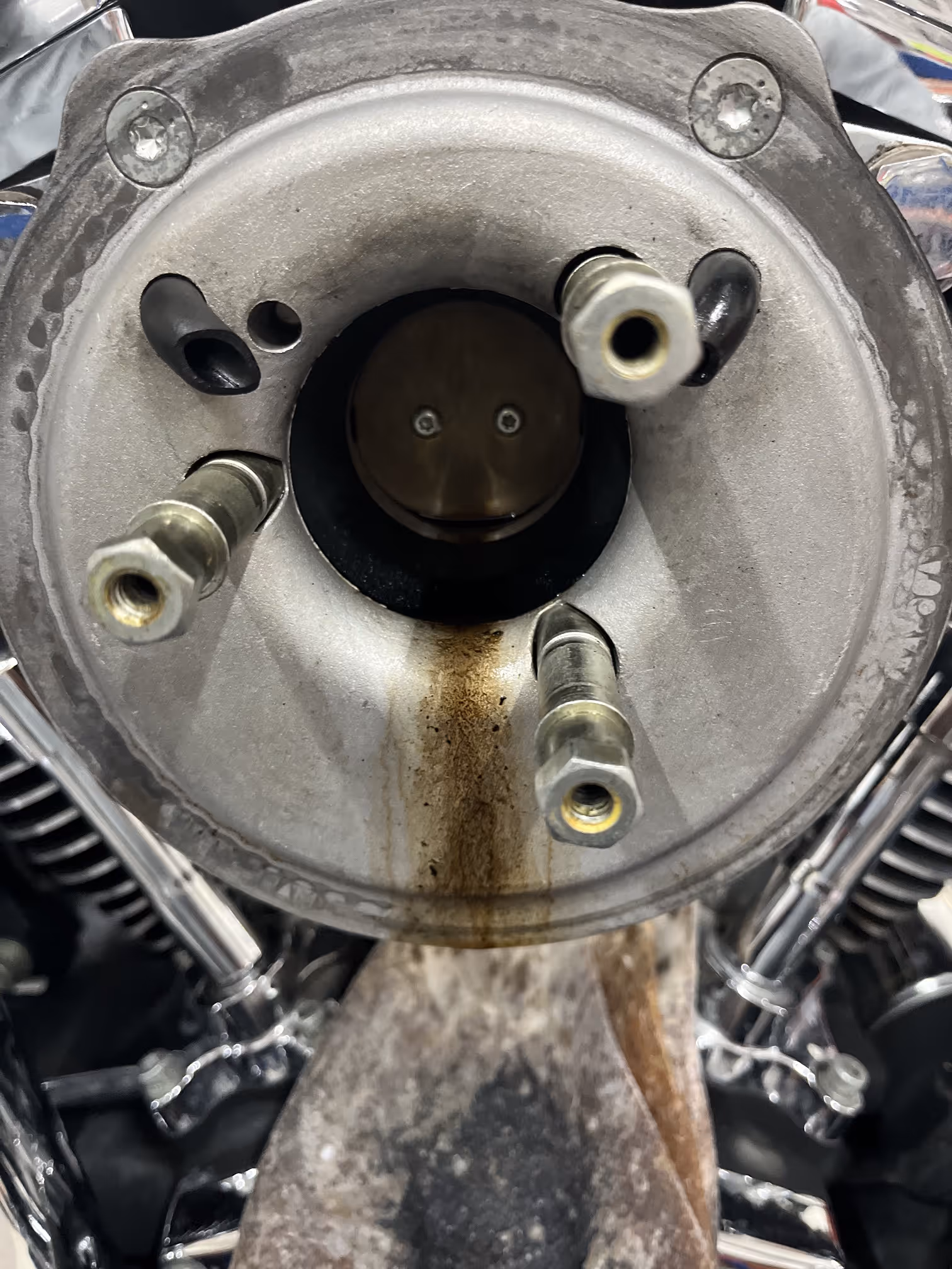 Close-up of a metallic engine component with three threaded studs and a central circular opening showing internal parts and oil stains.