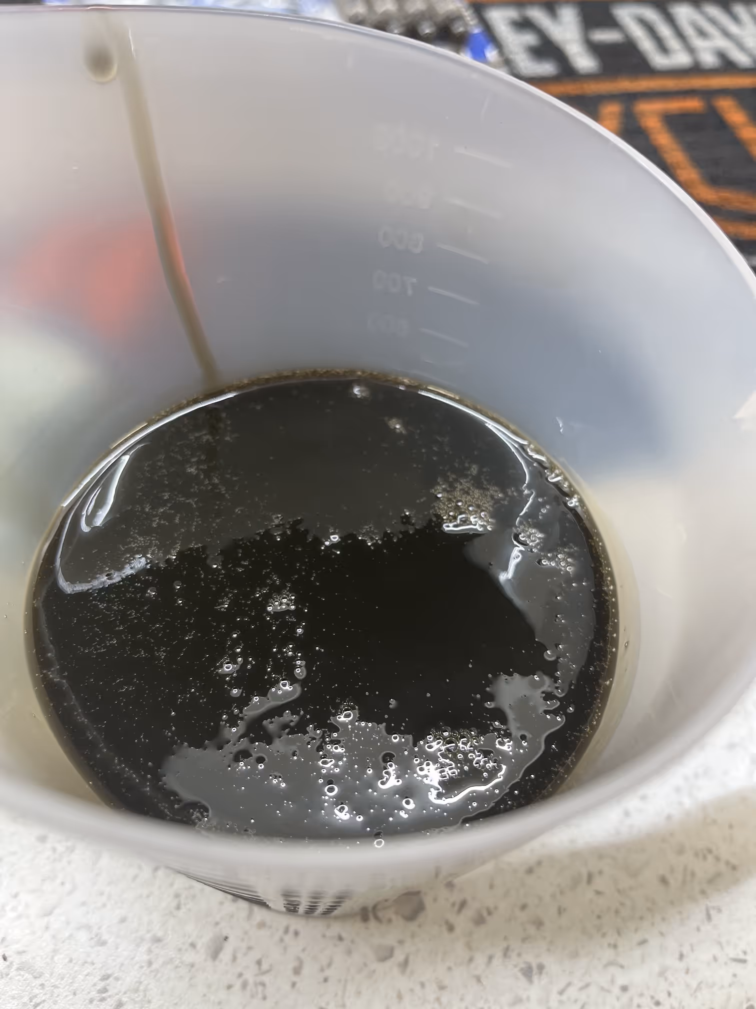 Close-up of a translucent measuring cup containing a dark liquid with small bubbles on the surface.