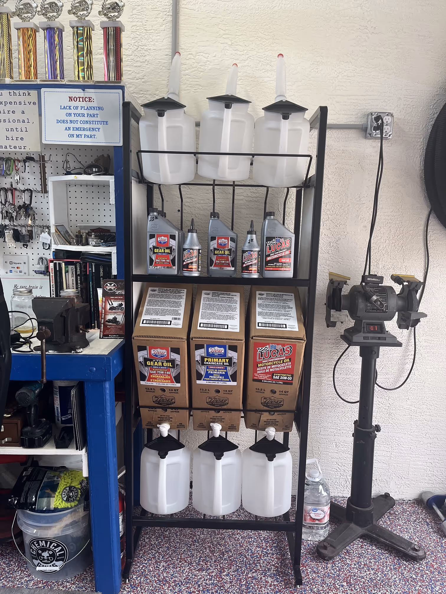 Metal rack with plastic oil containers and cardboard boxes of Lucas motorcycle and gear oils in a garage workspace.