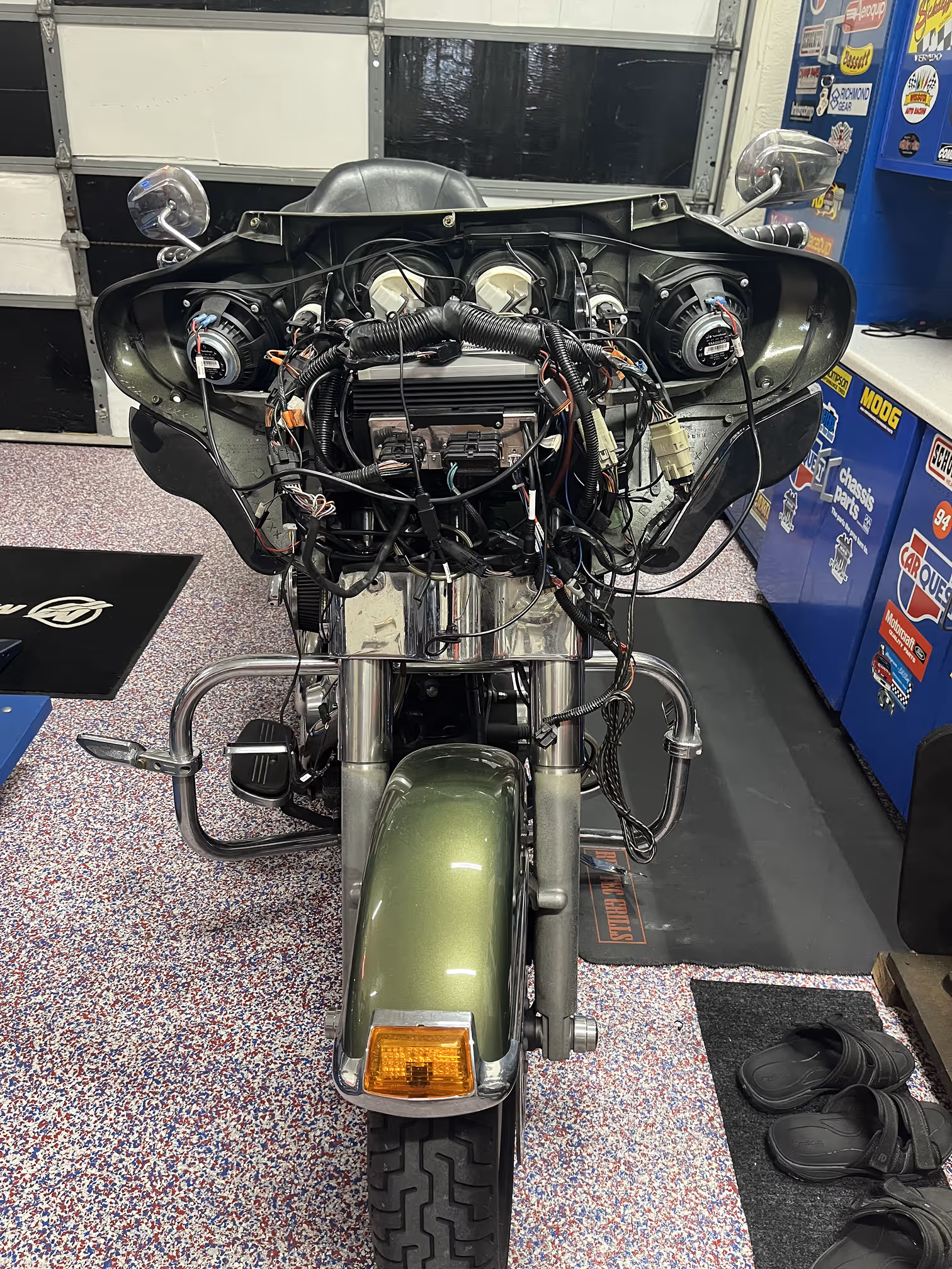 Front view of a motorcycle with exposed wiring and dashboard components in a garage setting.