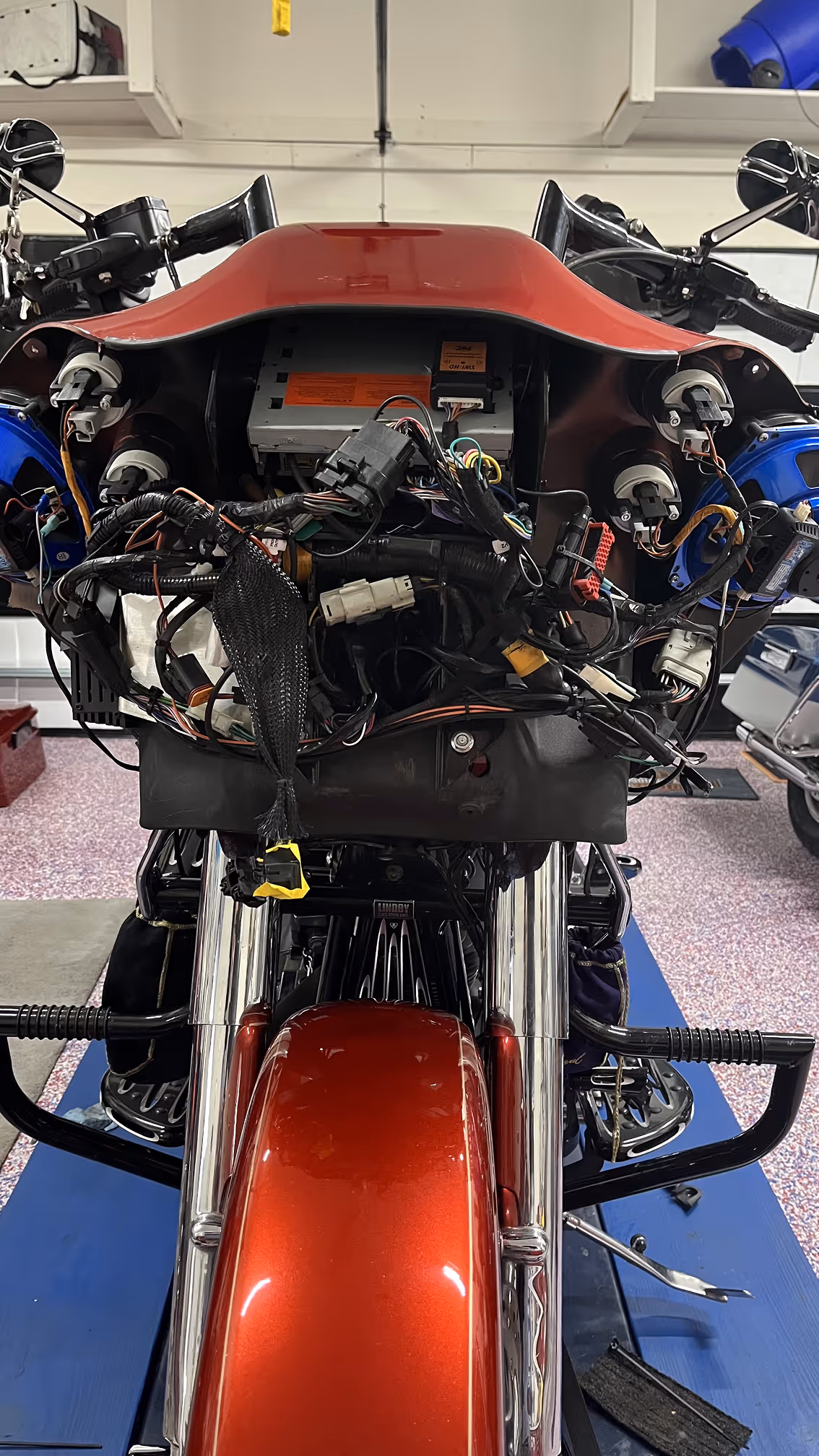 Close-up front view of a motorcycle with the dashboard and wiring exposed during repair in a garage.