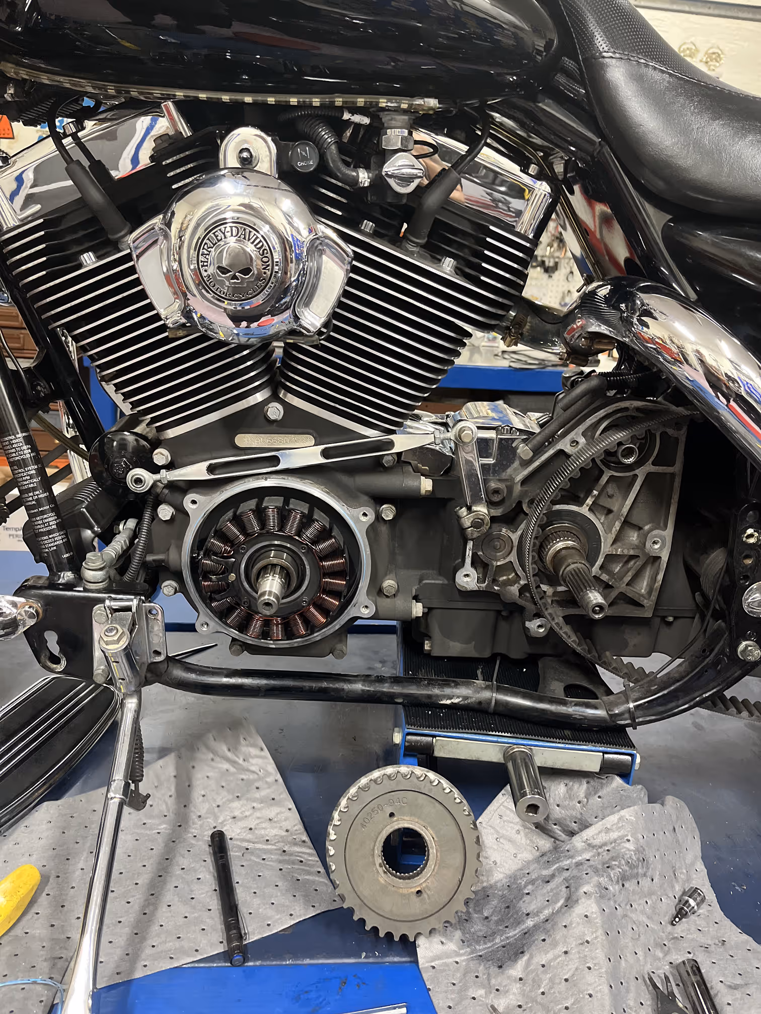 Close-up of a disassembled Harley-Davidson motorcycle engine with visible belts, gears, and chrome parts on a workbench.