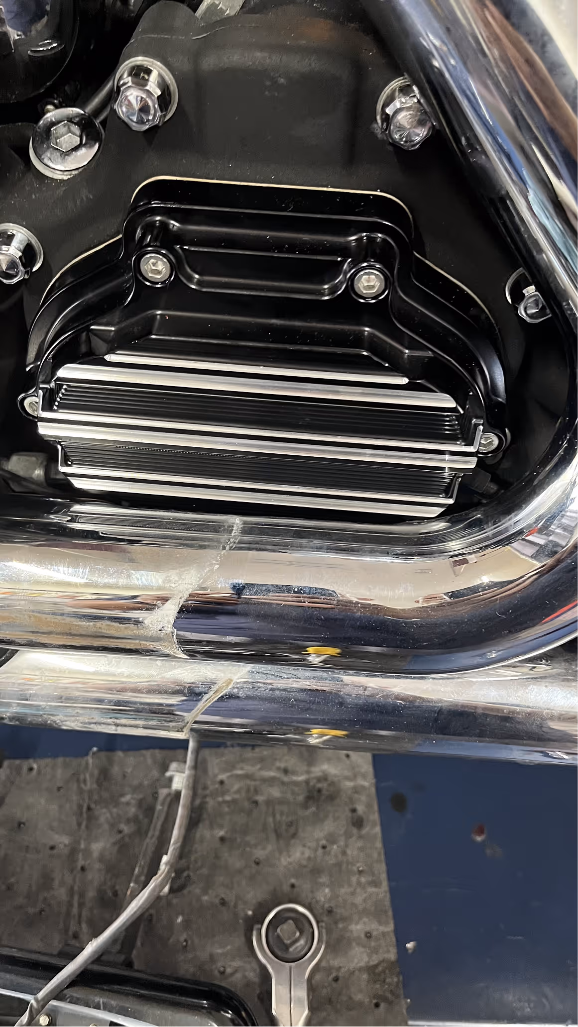 Close-up of a motorcycle engine part with chrome exhaust pipes and a wrench resting below on the ground.