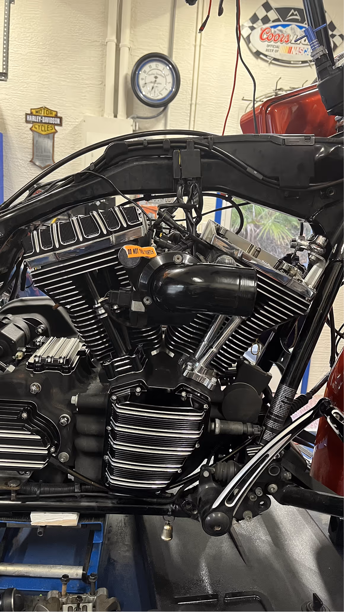 Close-up of a black and chrome Harley-Davidson motorcycle engine inside a workshop with a Harley-Davidson sign and a round clock on the wall.