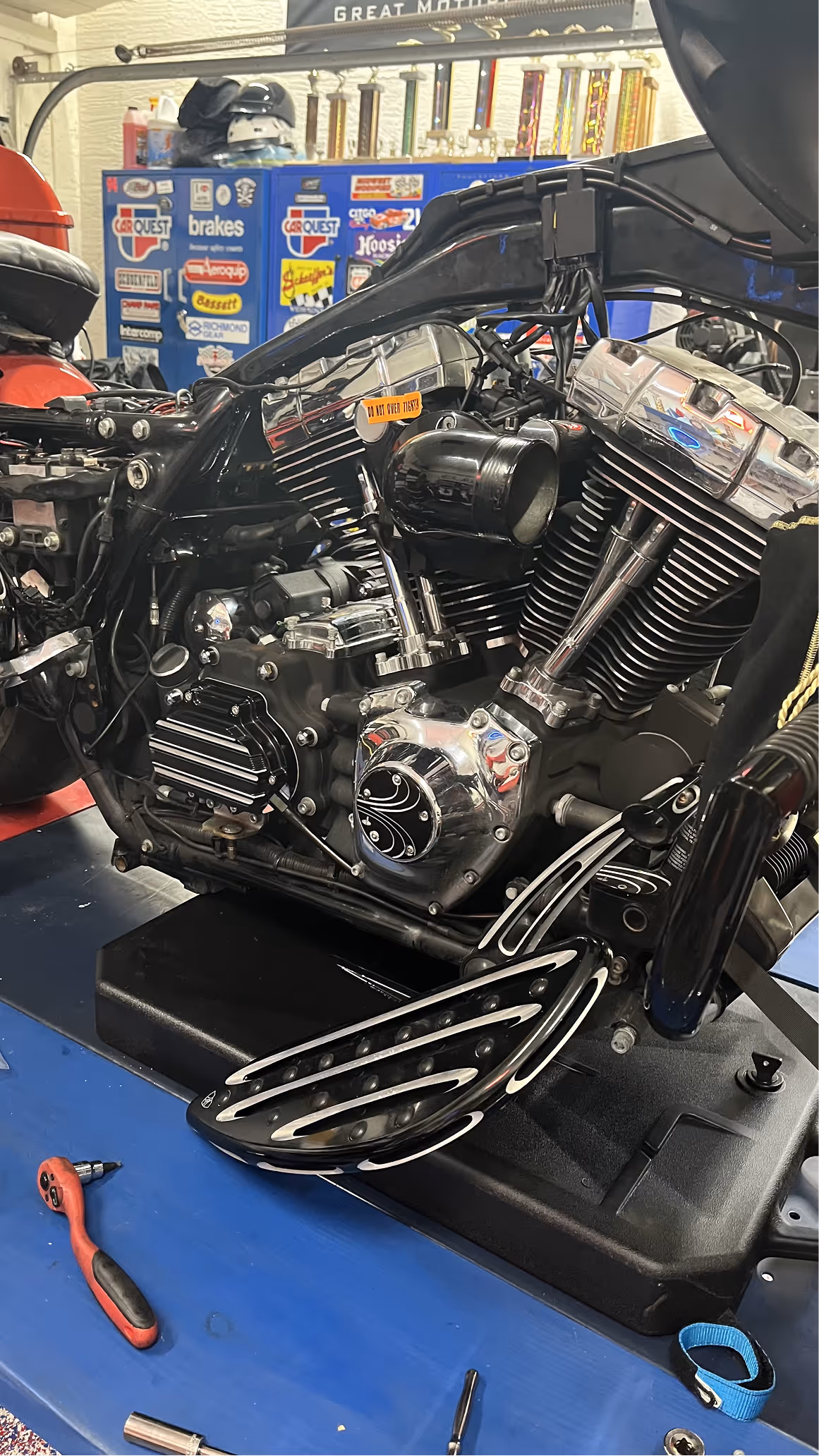 Close-up of a black motorcycle engine with chrome details on a blue workbench with tools.