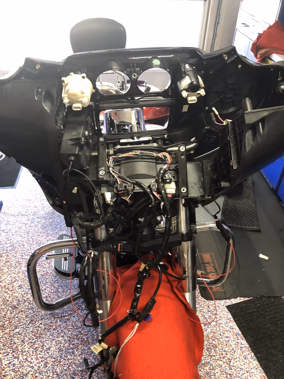 Front view of a motorcycle with its dashboard and wiring exposed and a red cloth covering the front fork.