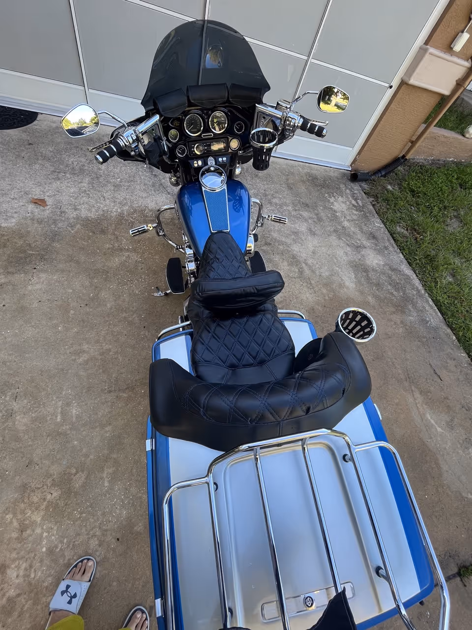 Top view of a blue and silver motorcycle with leather seat and two handlebars, parked on concrete near a garage door.