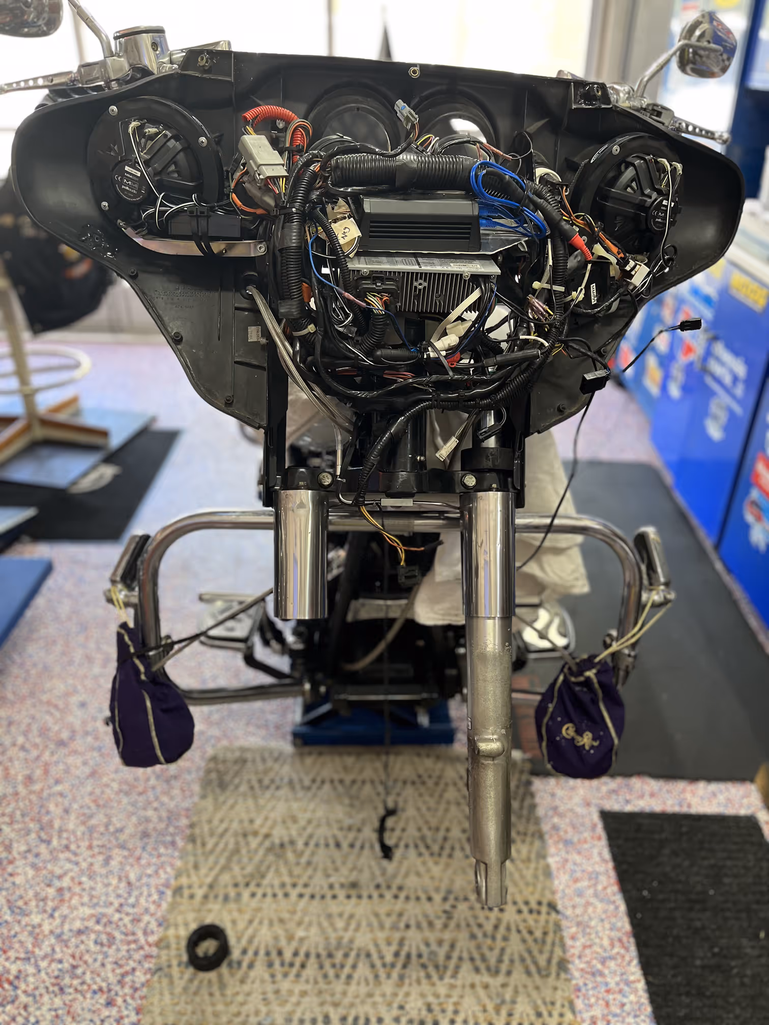 Front view of a motorcycle dashboard frame with exposed wiring and speakers in a workshop.