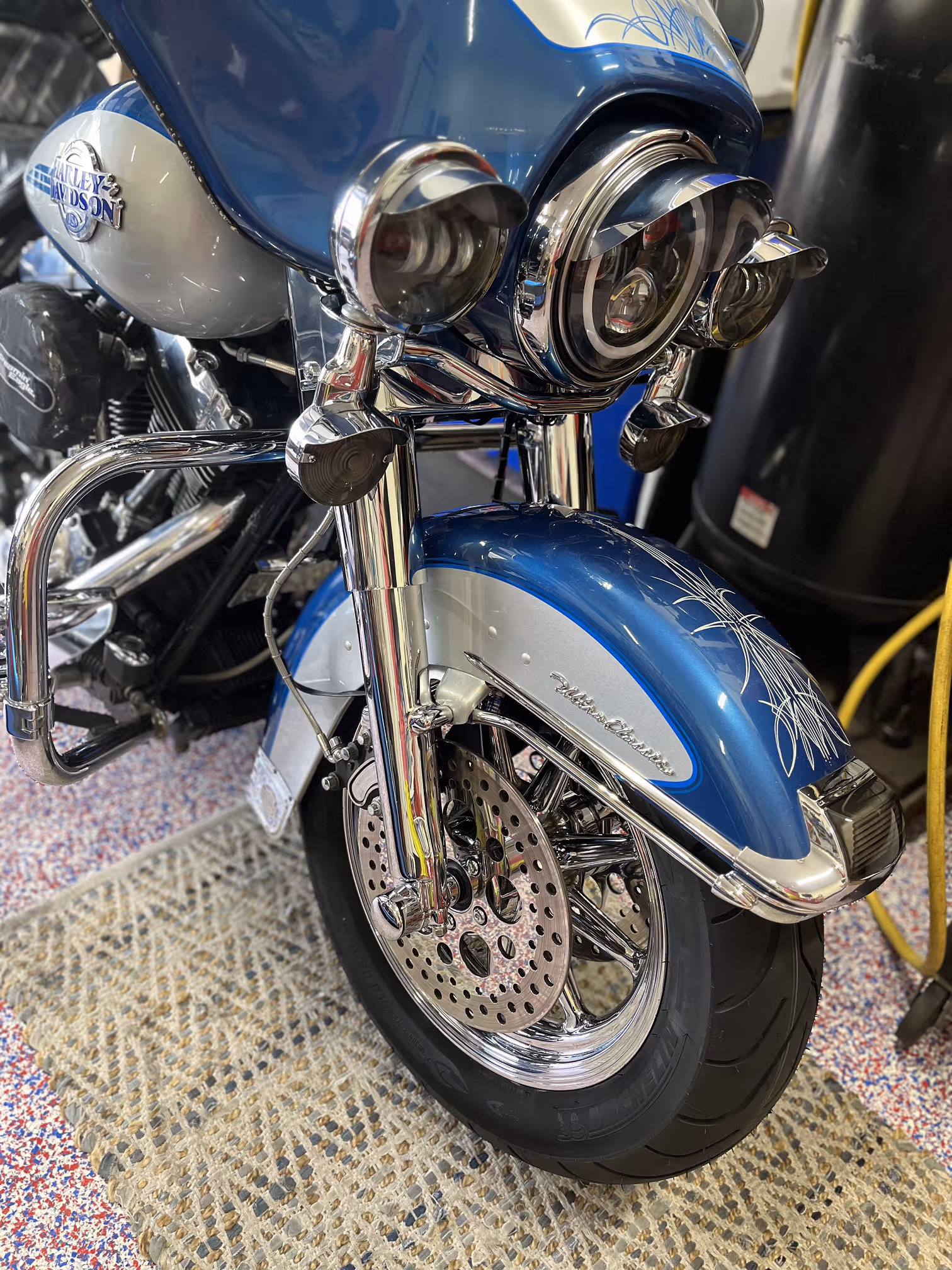 Close-up of the front wheel and fender of a blue and white Harley-Davidson motorcycle with chrome details and dual headlights.