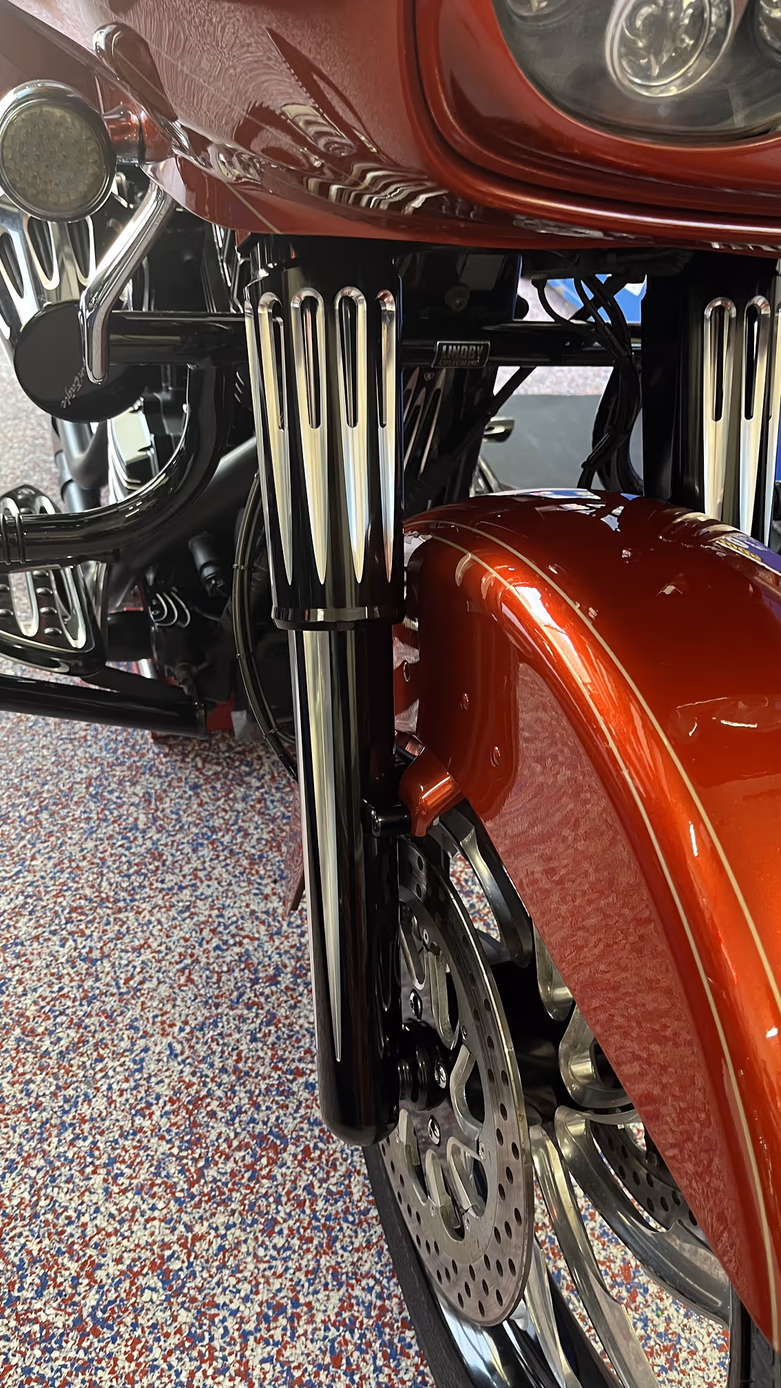 Close-up front view of a motorcycle suspension and front wheel with a shiny red fender and detailed chrome fork covers.