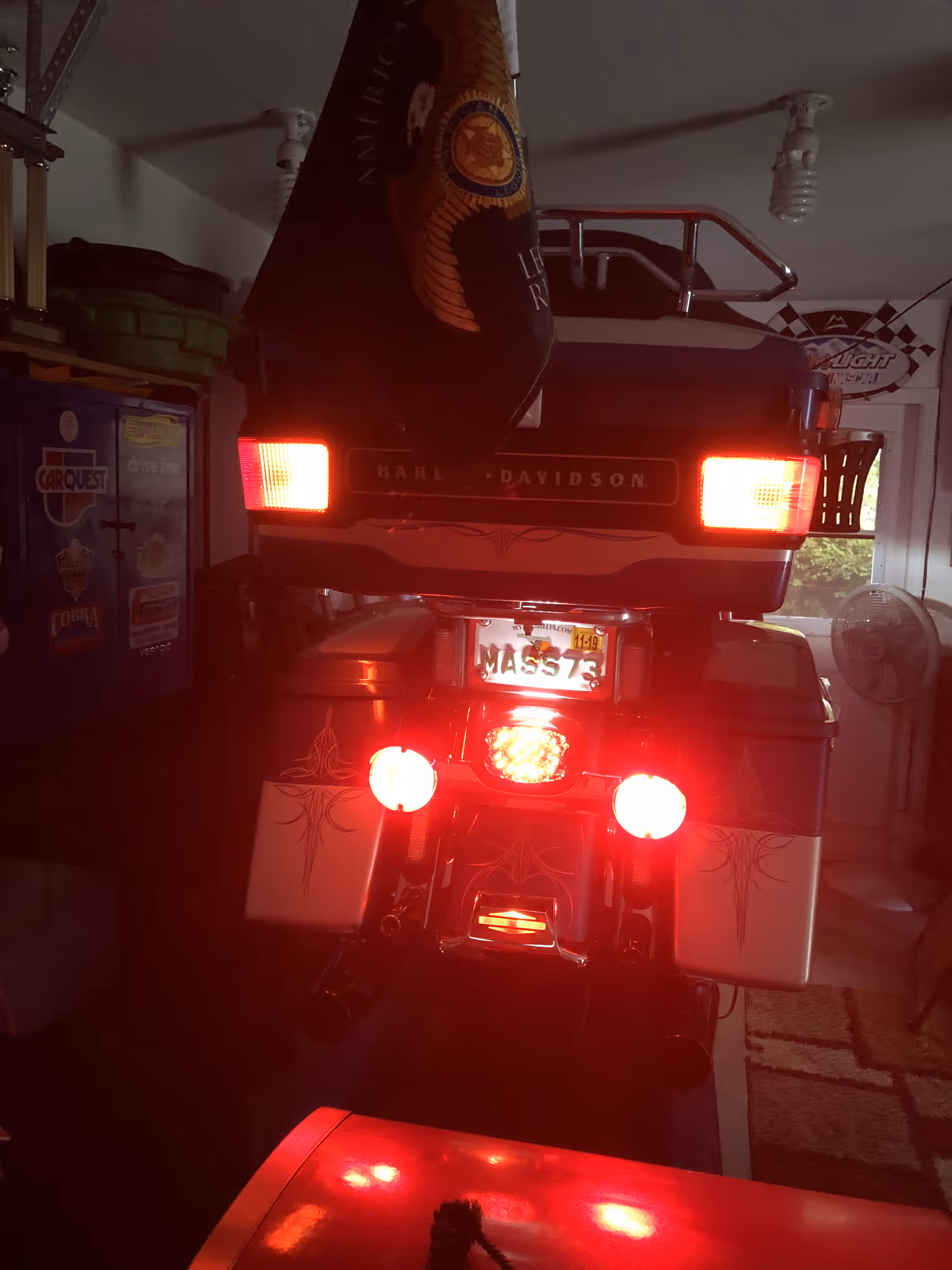 Rear view of a Harley-Davidson motorcycle with illuminated red brake lights and Massachusetts license plate inside a garage.