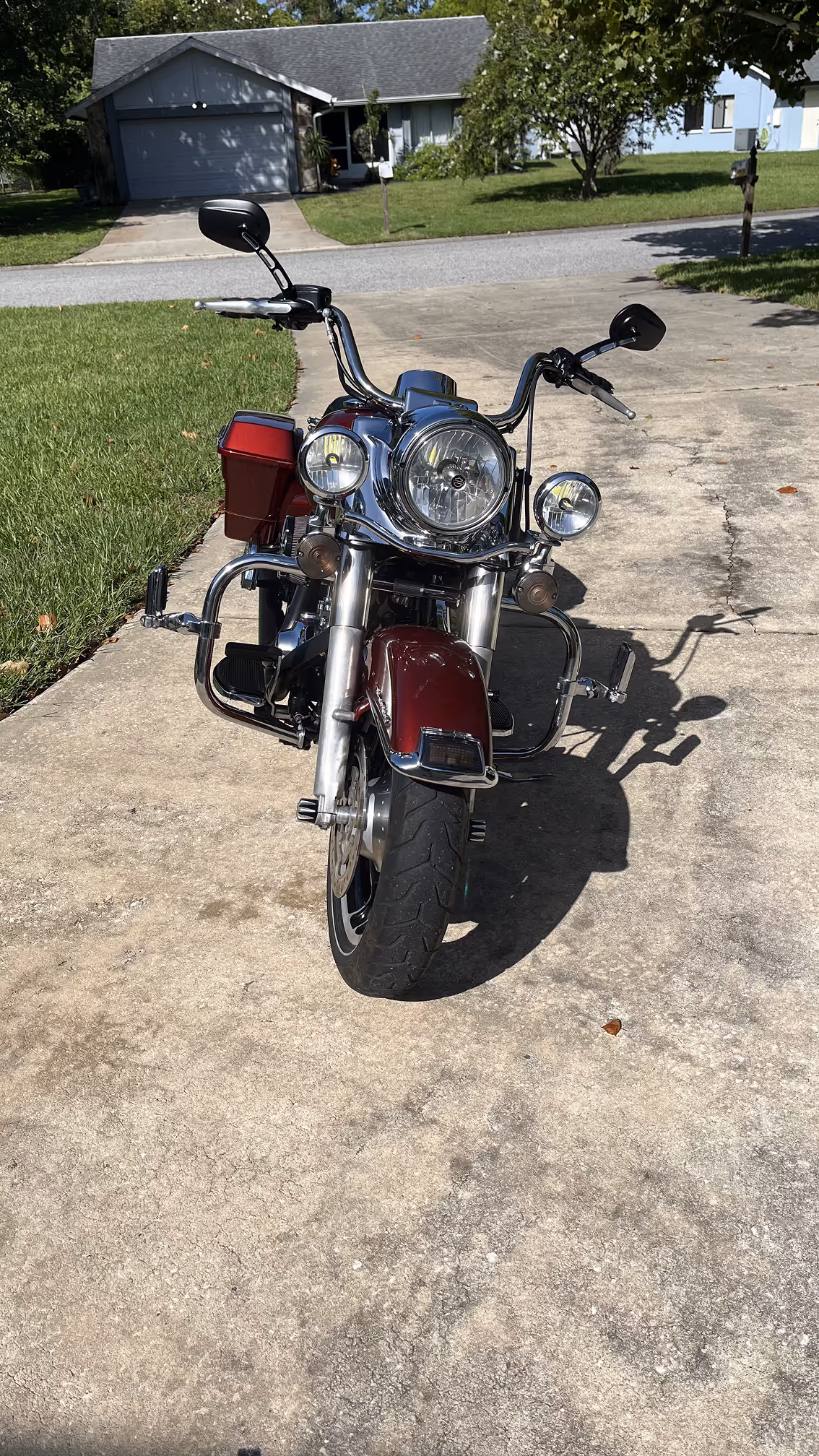 Front view of a maroon and chrome cruiser motorcycle parked on a concrete driveway with grass and houses in the background.