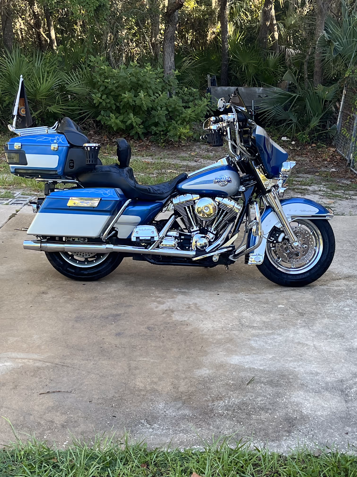 Blue and silver Harley-Davidson touring motorcycle parked on concrete with greenery in background.