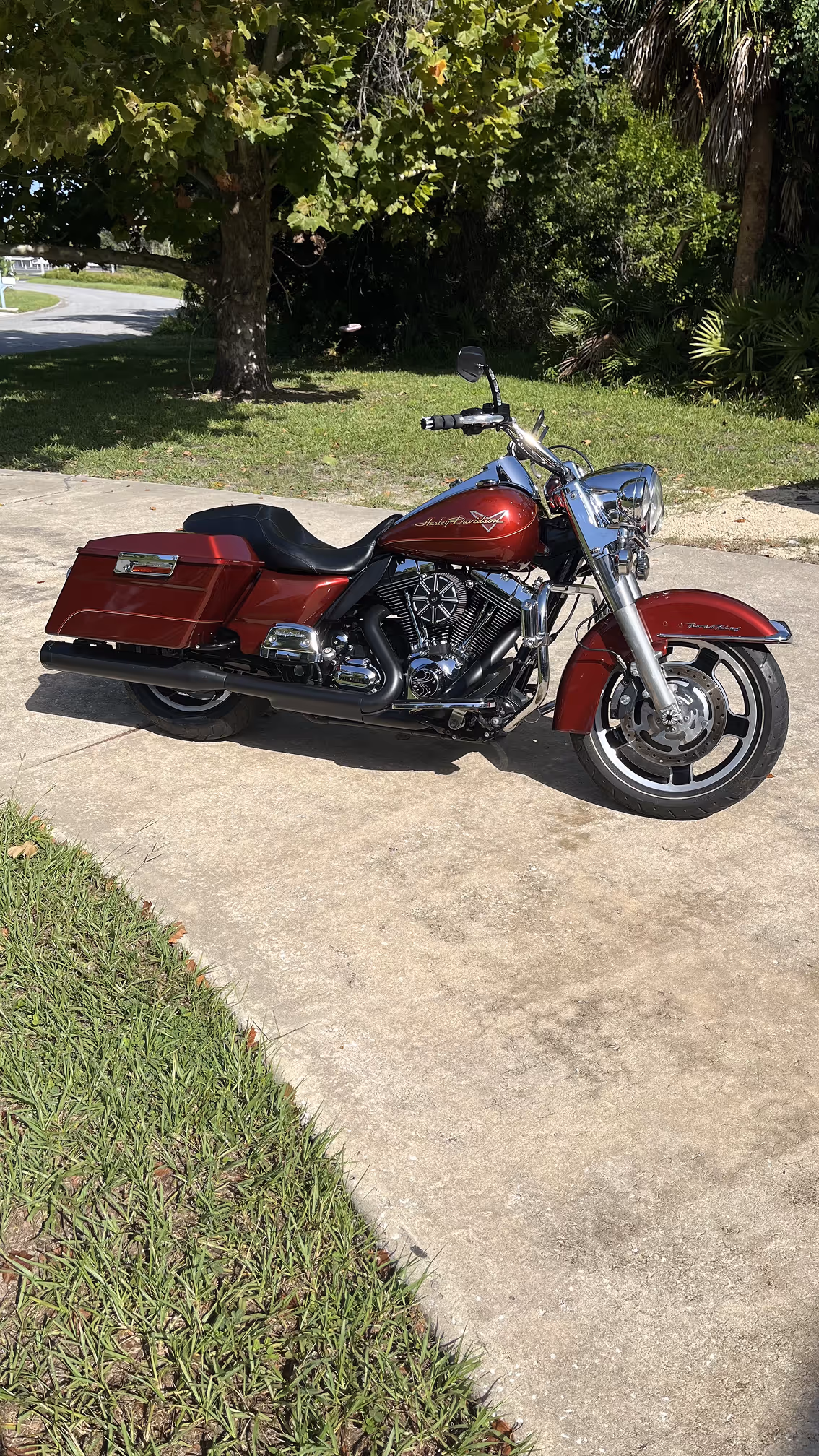 Red Harley-Davidson touring motorcycle parked on a concrete driveway with grass and trees in the background.