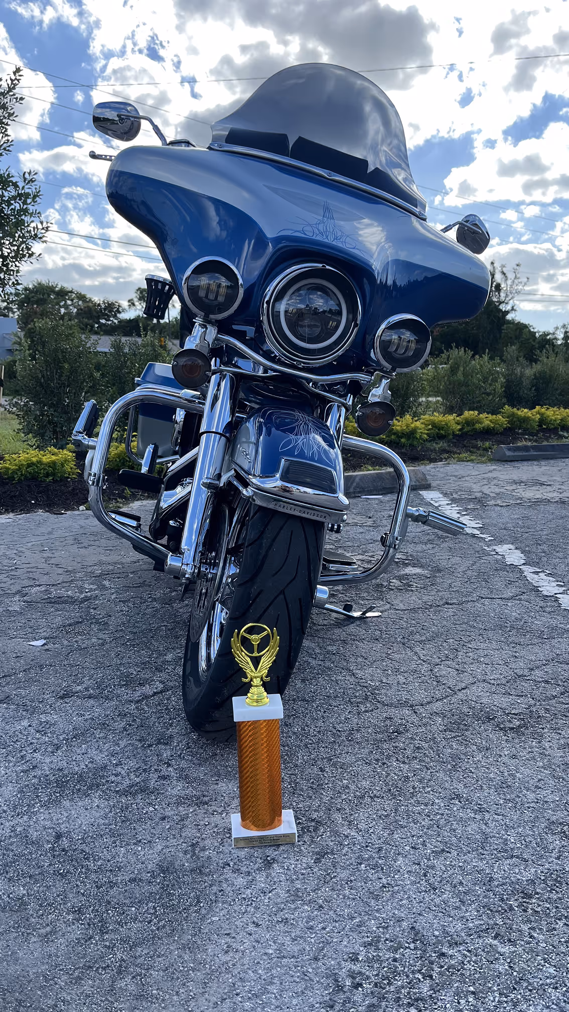 Blue Harley-Davidson motorcycle parked outdoors with a gold trophy placed in front of its front tire.