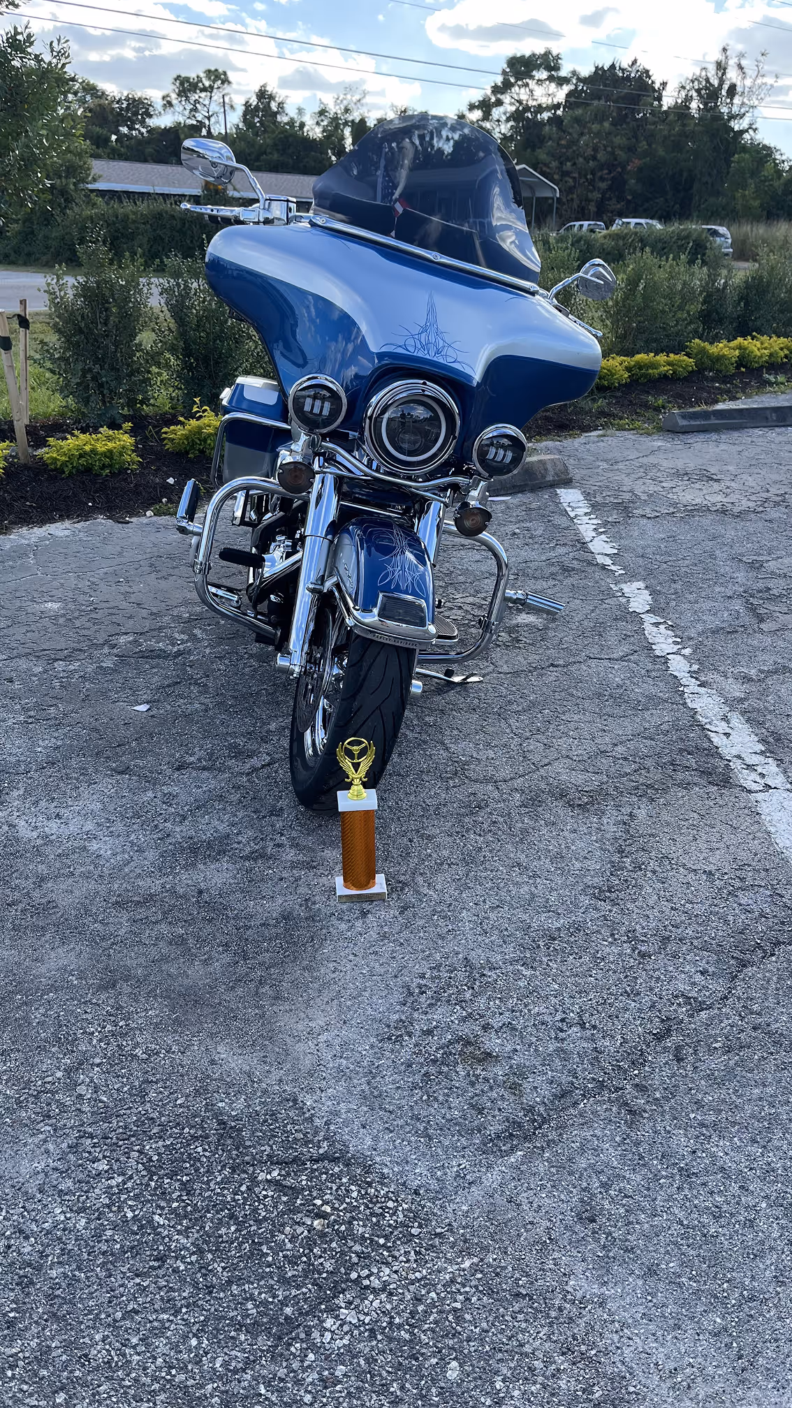 Blue touring motorcycle with chrome details parked on asphalt with a trophy placed in front of the front tire.