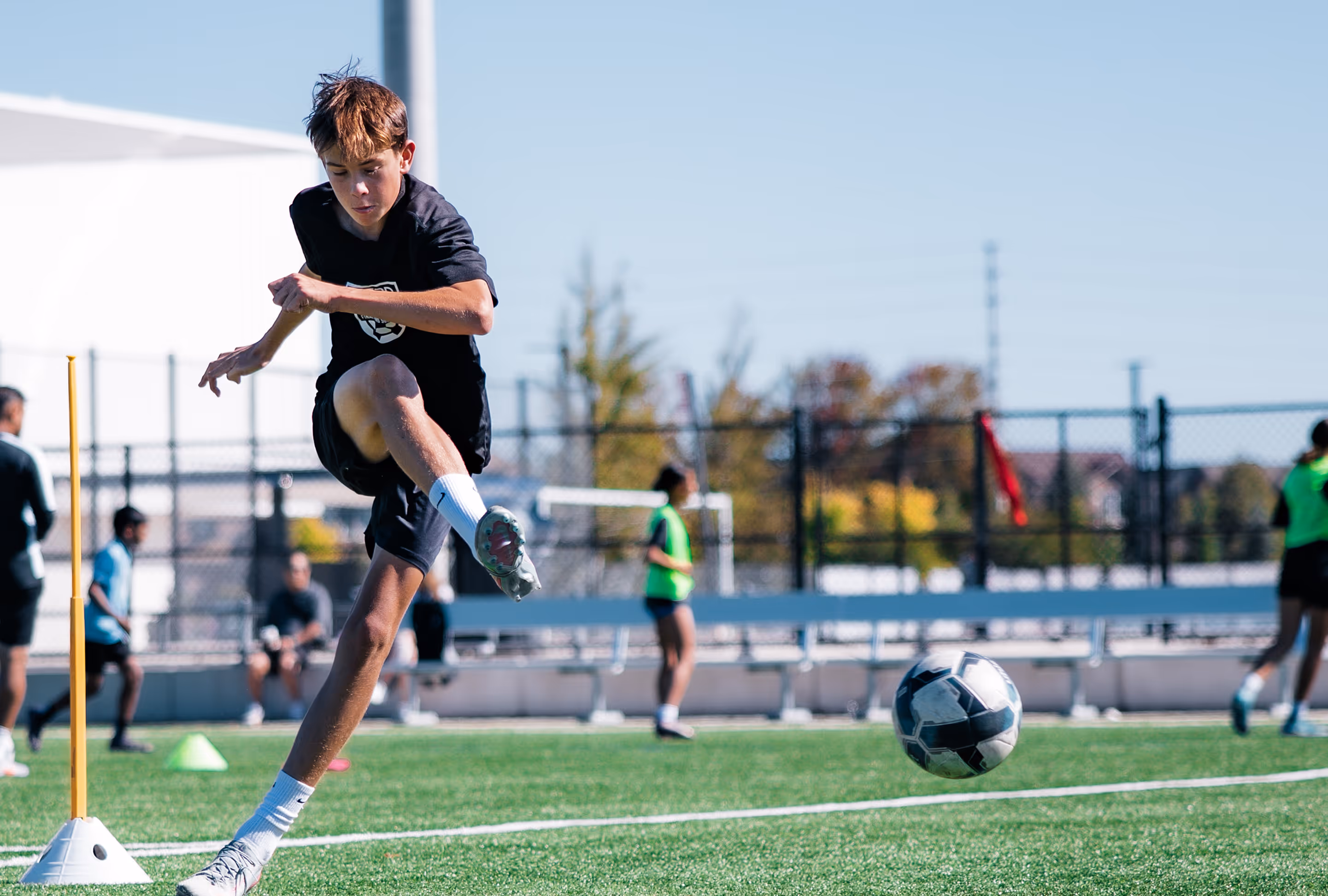 Young soccer player in black kicking a soccer ball during outdoor practice on a green field.