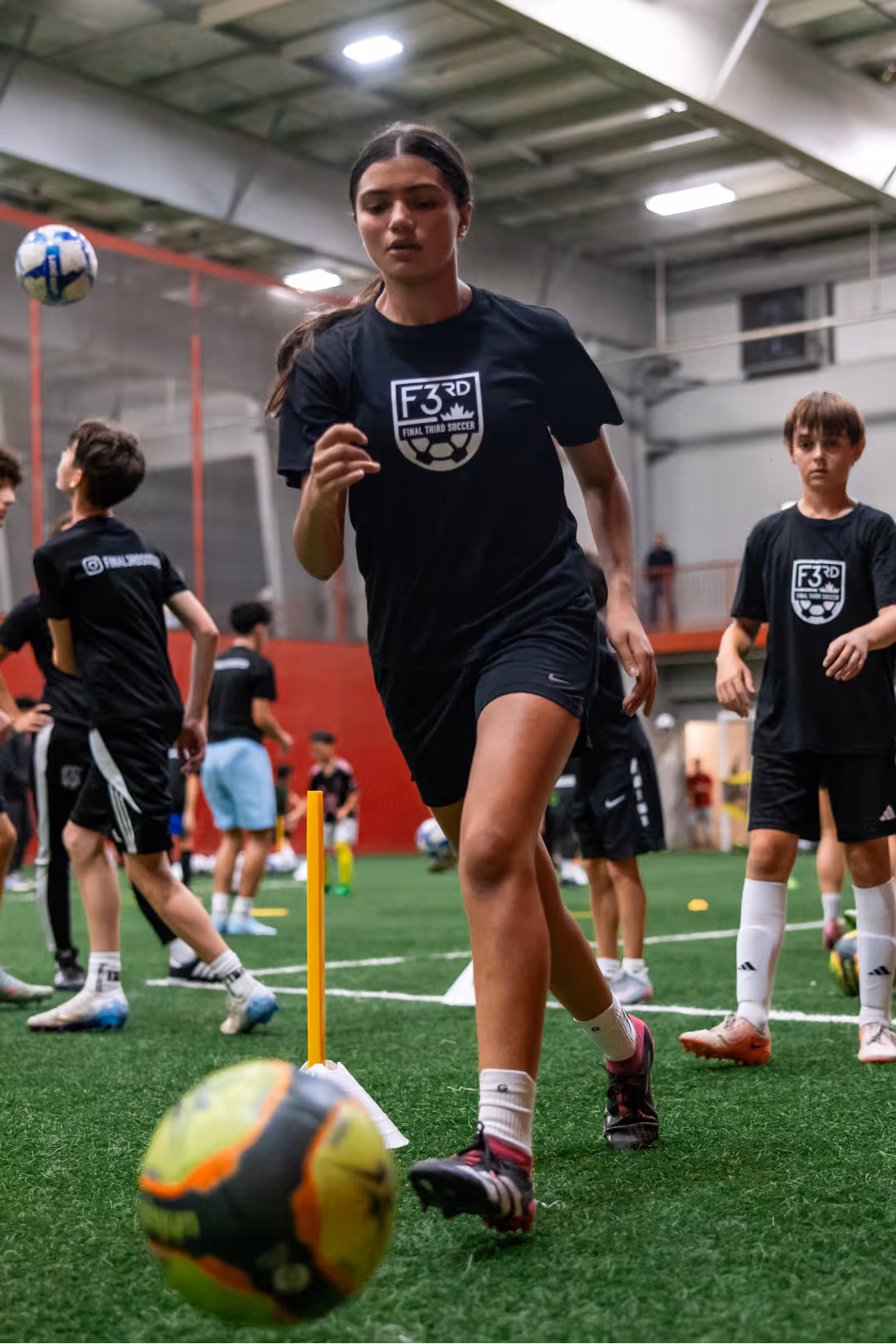 Young soccer players training indoors on artificial grass, wearing black F3RD Final Third Soccer shirts.