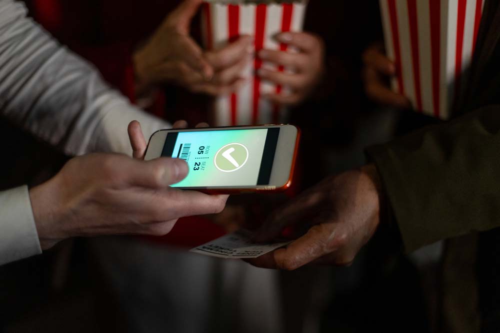 Person holding a smartphone with a digital movie ticket while holding a popcorn bucket