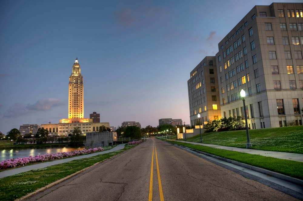 Nighttime street-level view of downtown Baton Rouge with the Louisiana State Capitol building illuminated in the background
