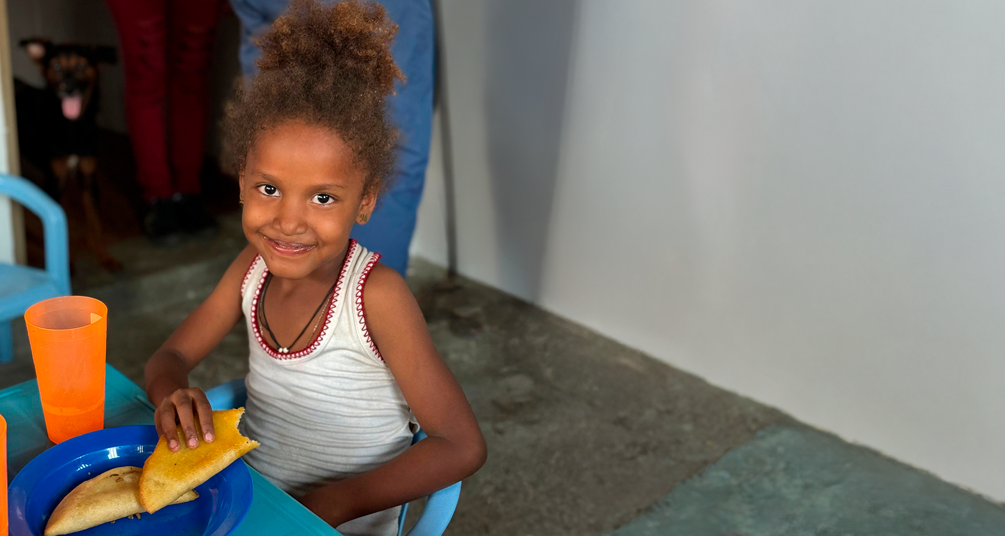 Smiling girl sitting at a table eating empanadas with orange cups nearby.