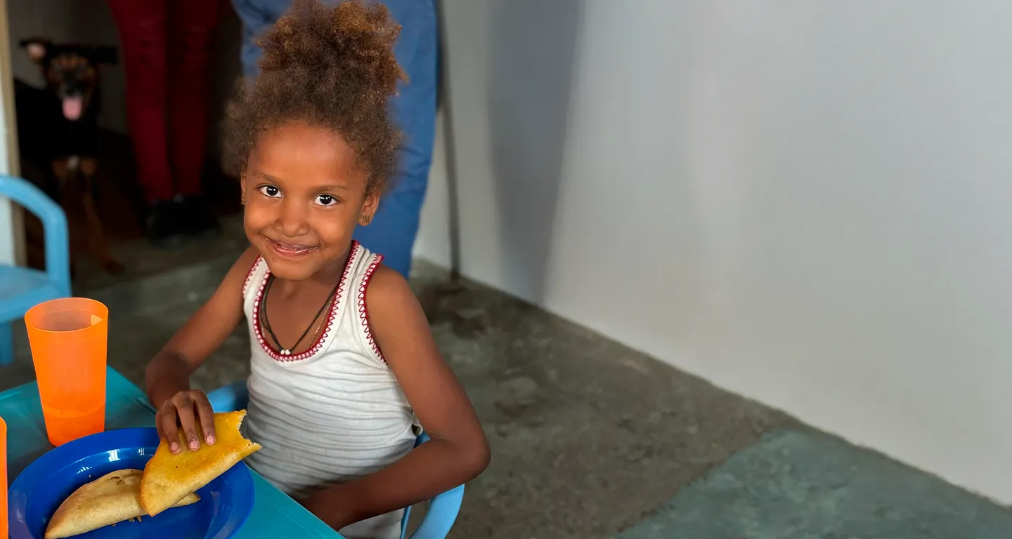 Smiling girl sitting at a table eating empanadas with orange cups nearby.