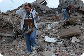A woman standing among the rubble of destroyed homes.