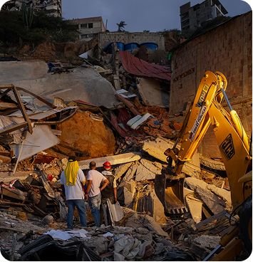 An excavator and workers clearing rubble from a collapsed building.