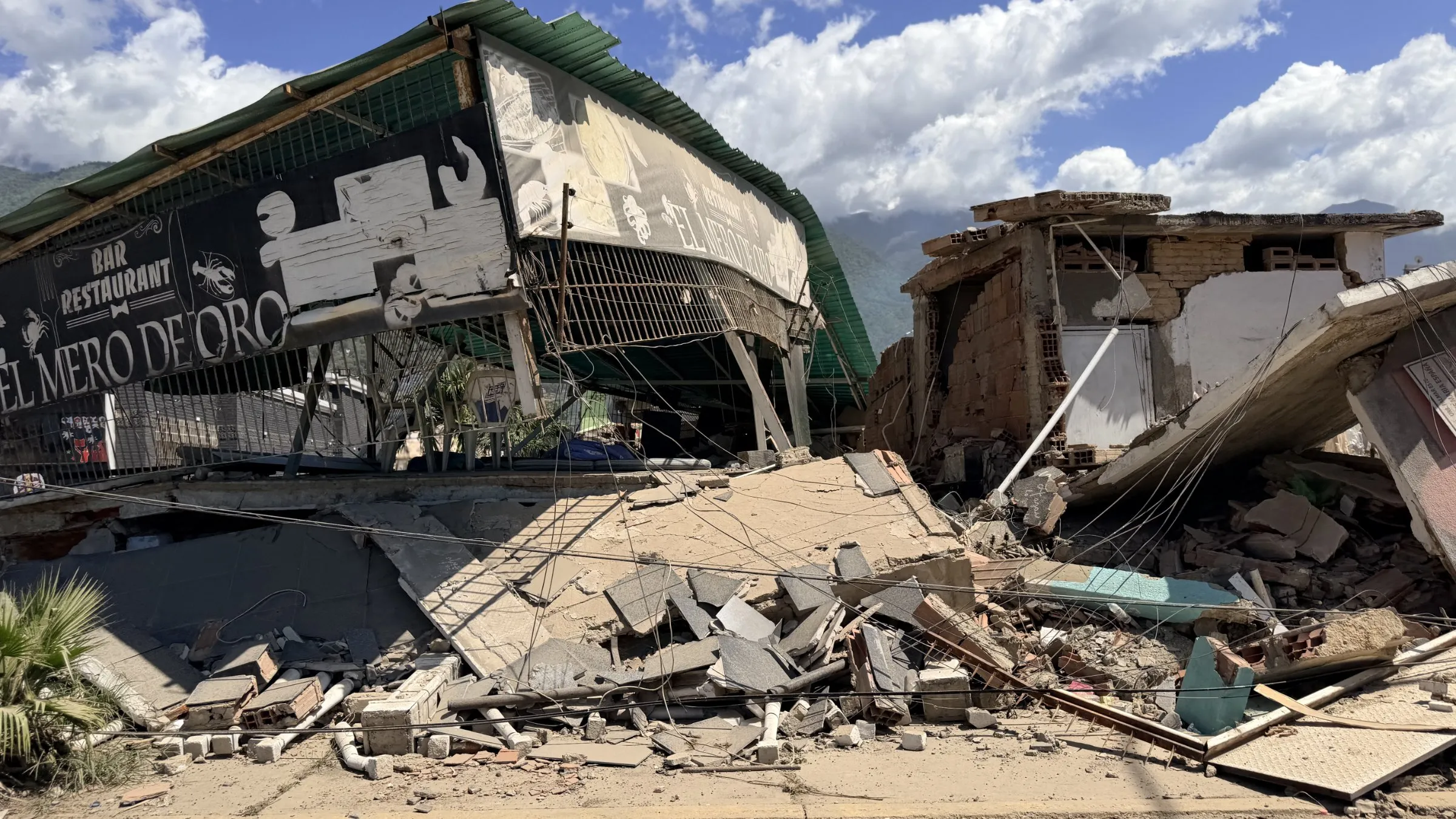 A building collapsed into rubble, with its upper floor hanging over the street.