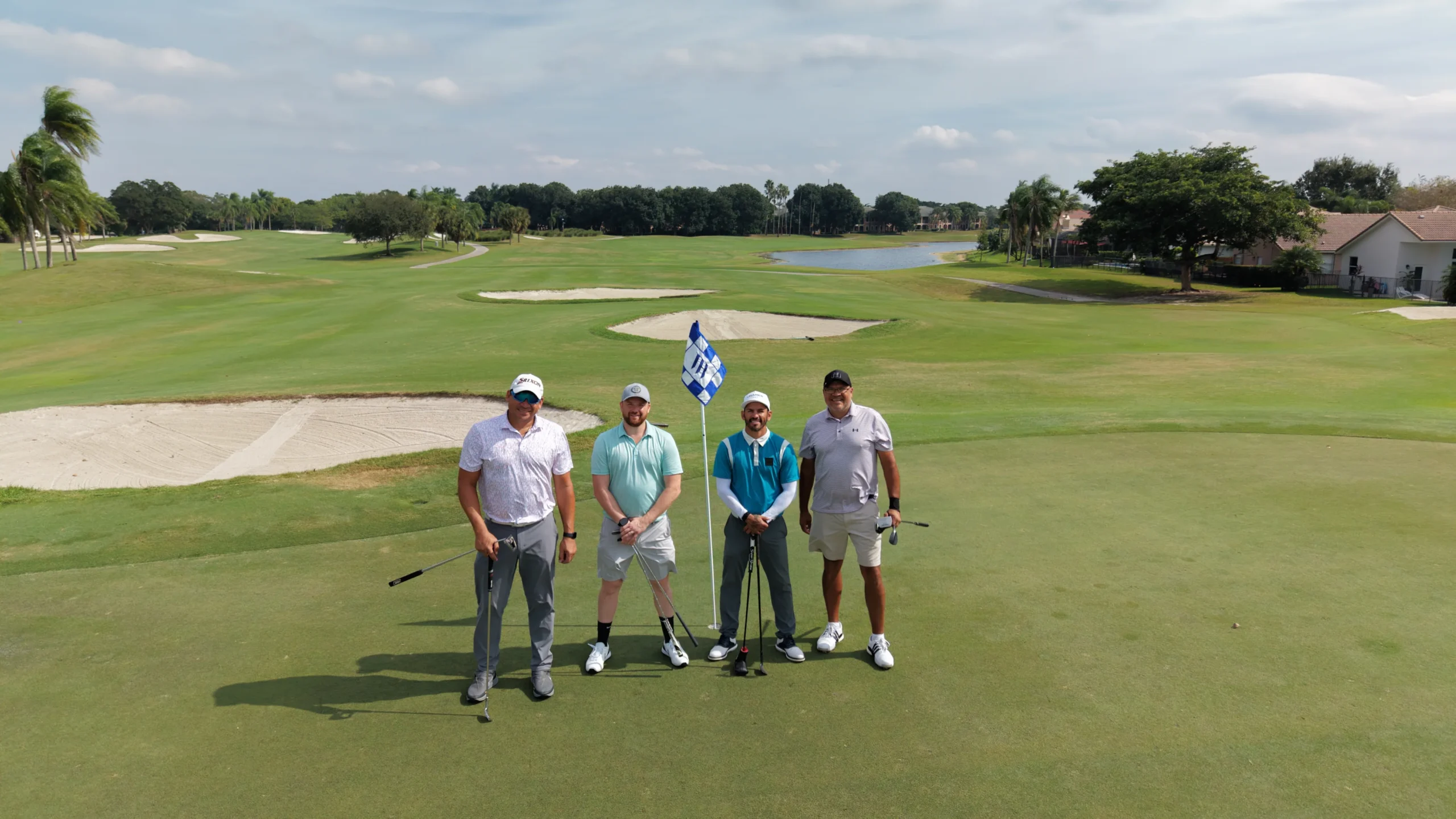 Cuatro golfistas en el tee, uno de ellos con una bandera de Venezuela.
