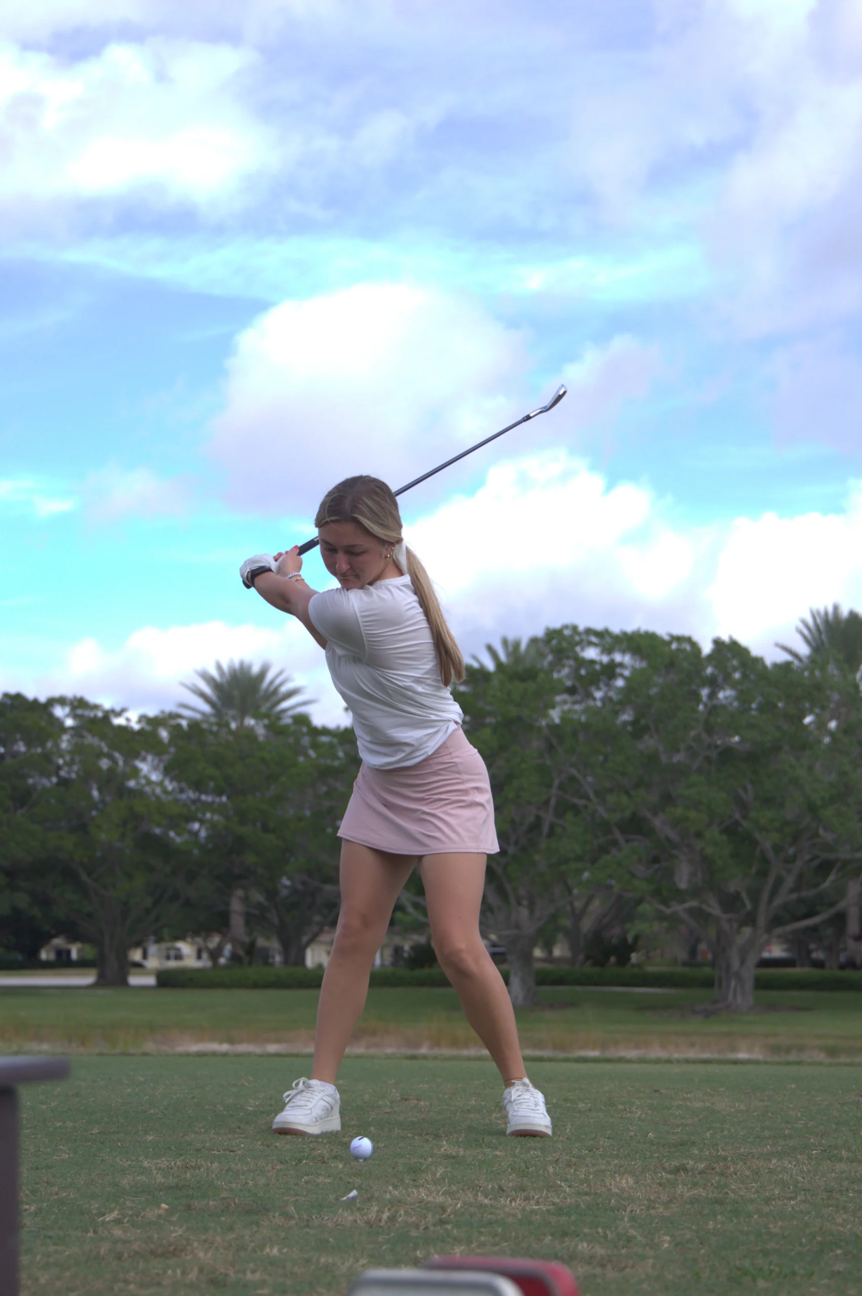 Una golfista termina su swing bajo un cielo despejado.