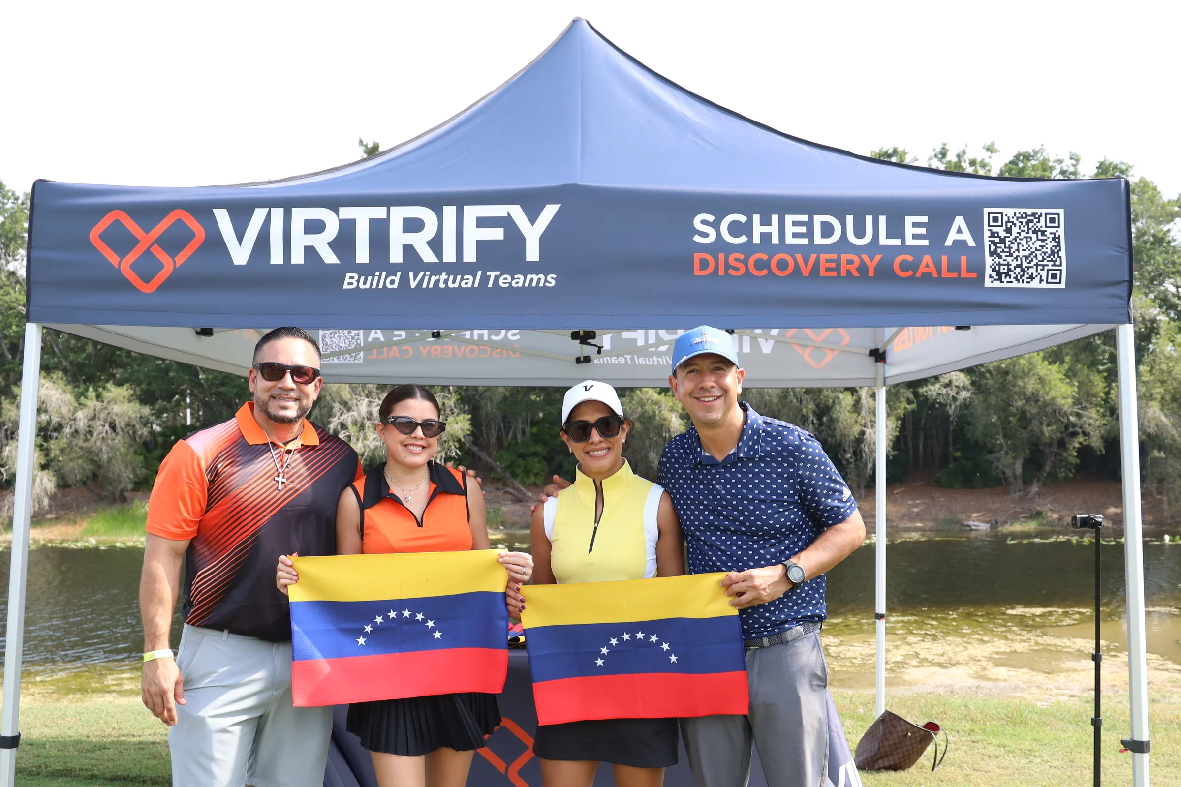 Tres participantes con banderas de Venezuela frente a la carpa de un patrocinador.