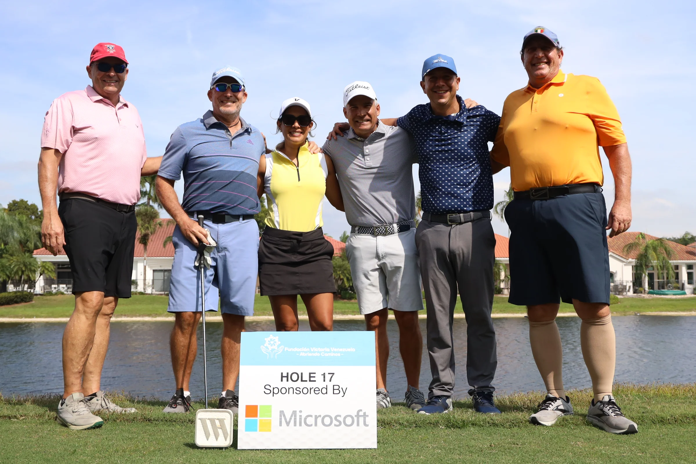 Un grupo de golfistas junto al letrero de un hoyo patrocinado.