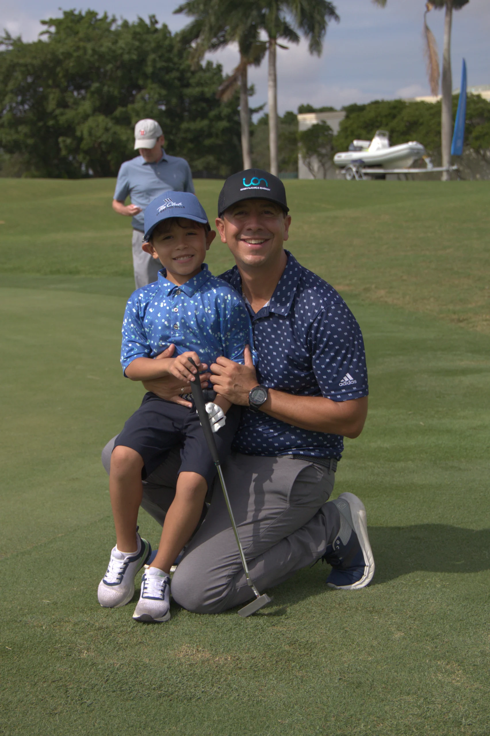 Un golfista arrodillado en el fairway junto a un niño que sostiene un palo.