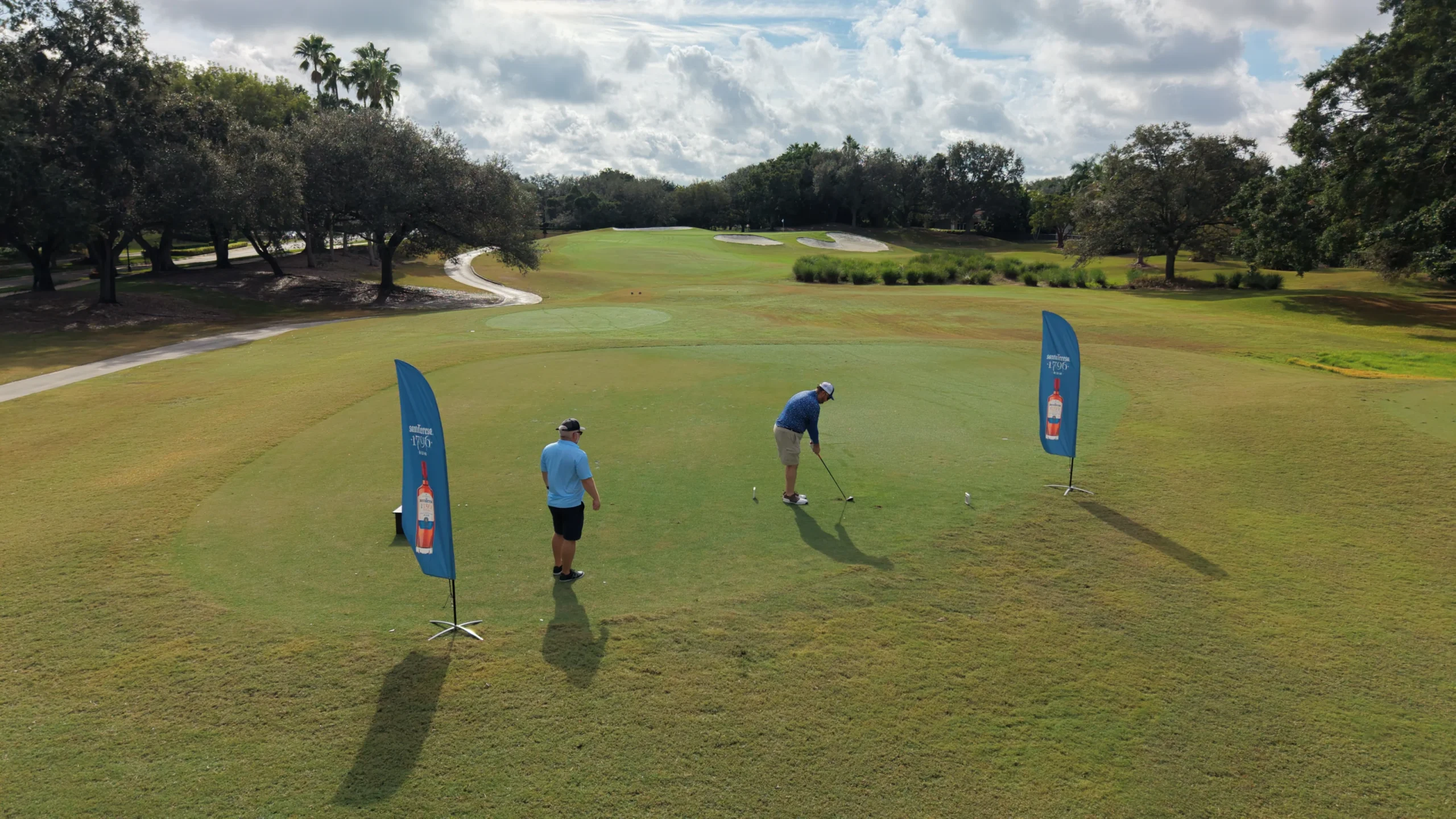 Dos golfistas juegan en el fairway, con pendones de la fundación a un lado.