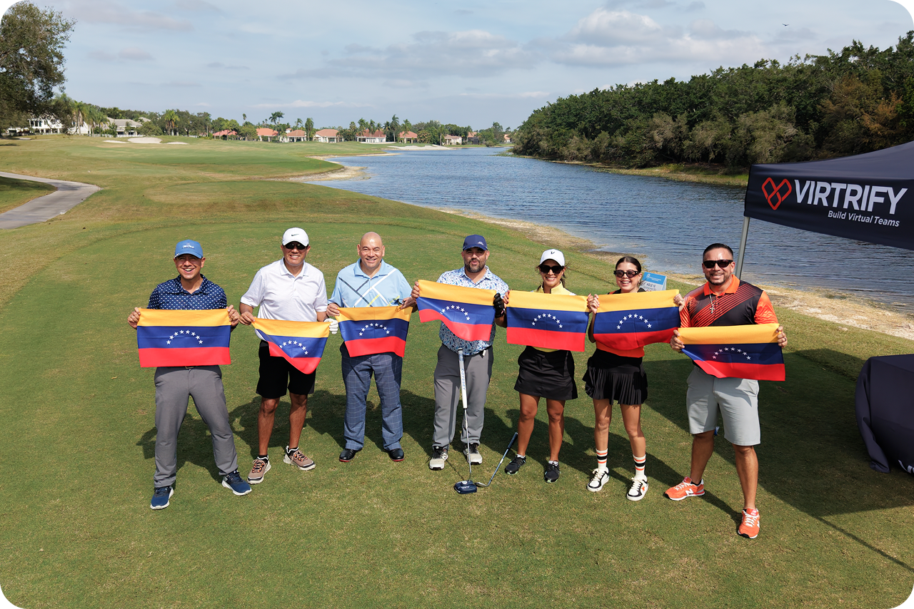 Seven golfers standing together on the course, each holding a Venezuelan flag, with the fairway and a lake behind them.