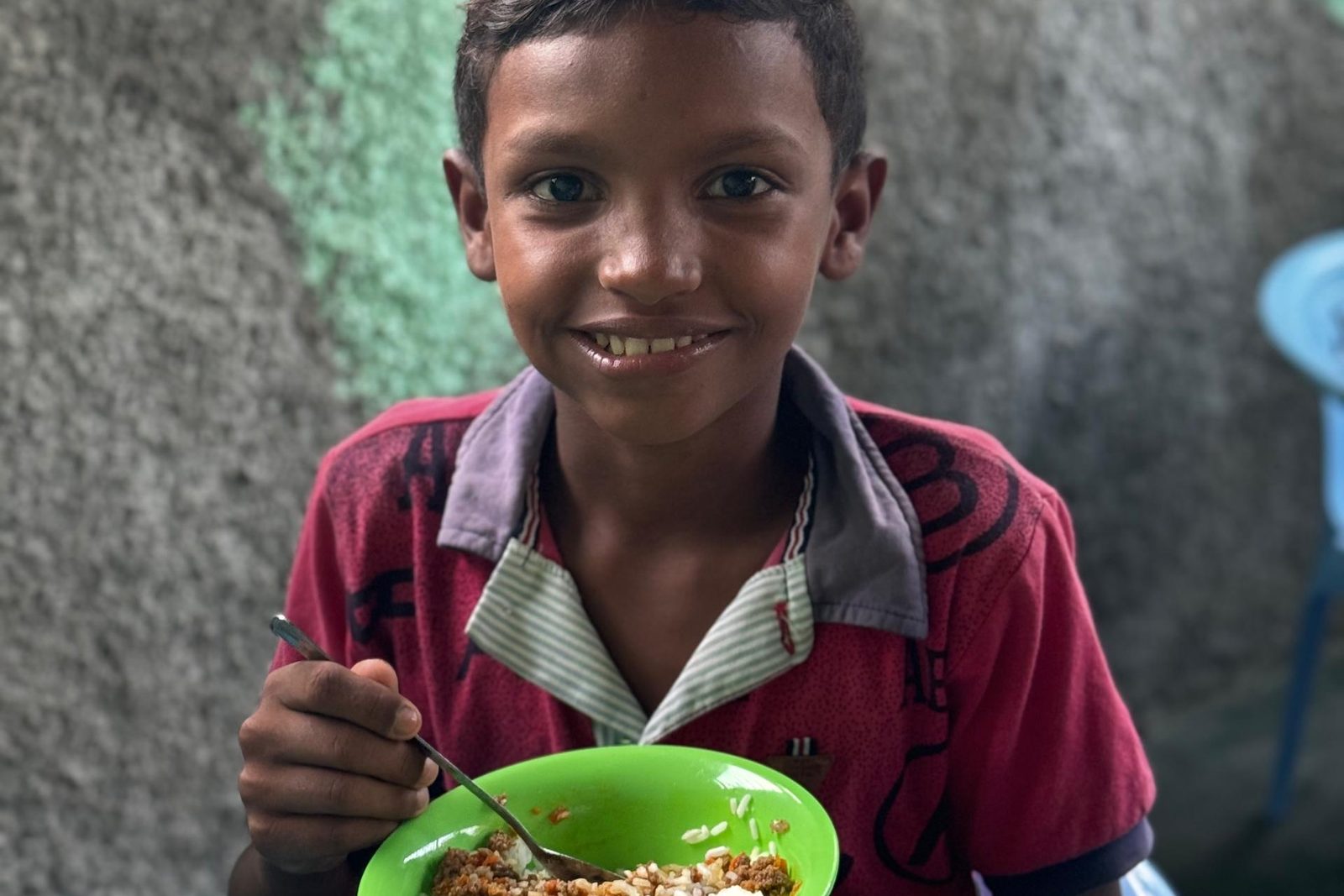 A boy in a red shirt eats lunch from a green bowl at a Victoria Venezuela Foundation meal program.