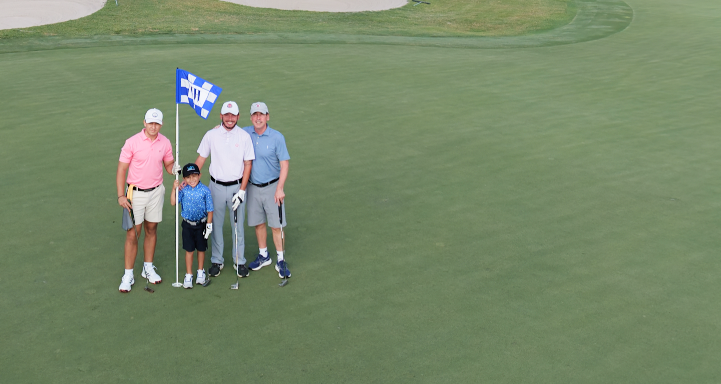 Three golfers and a young boy standing by the flag on the green.