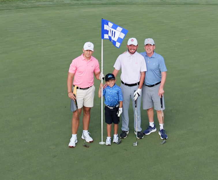 Three golfers and a young boy standing by the flag on the green.