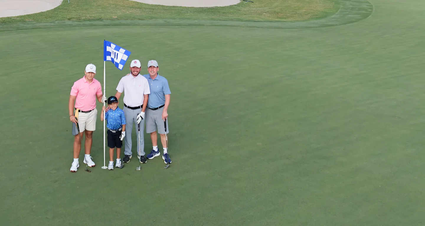 Three golfers and a young boy standing by the flag on the green.