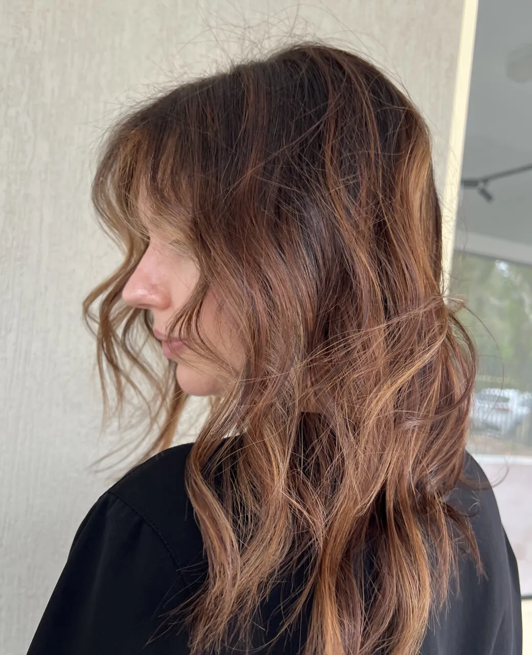 Side profile showing warm brown tint colour with subtle caramel tones through wavy mid-length hair by Jura Draco