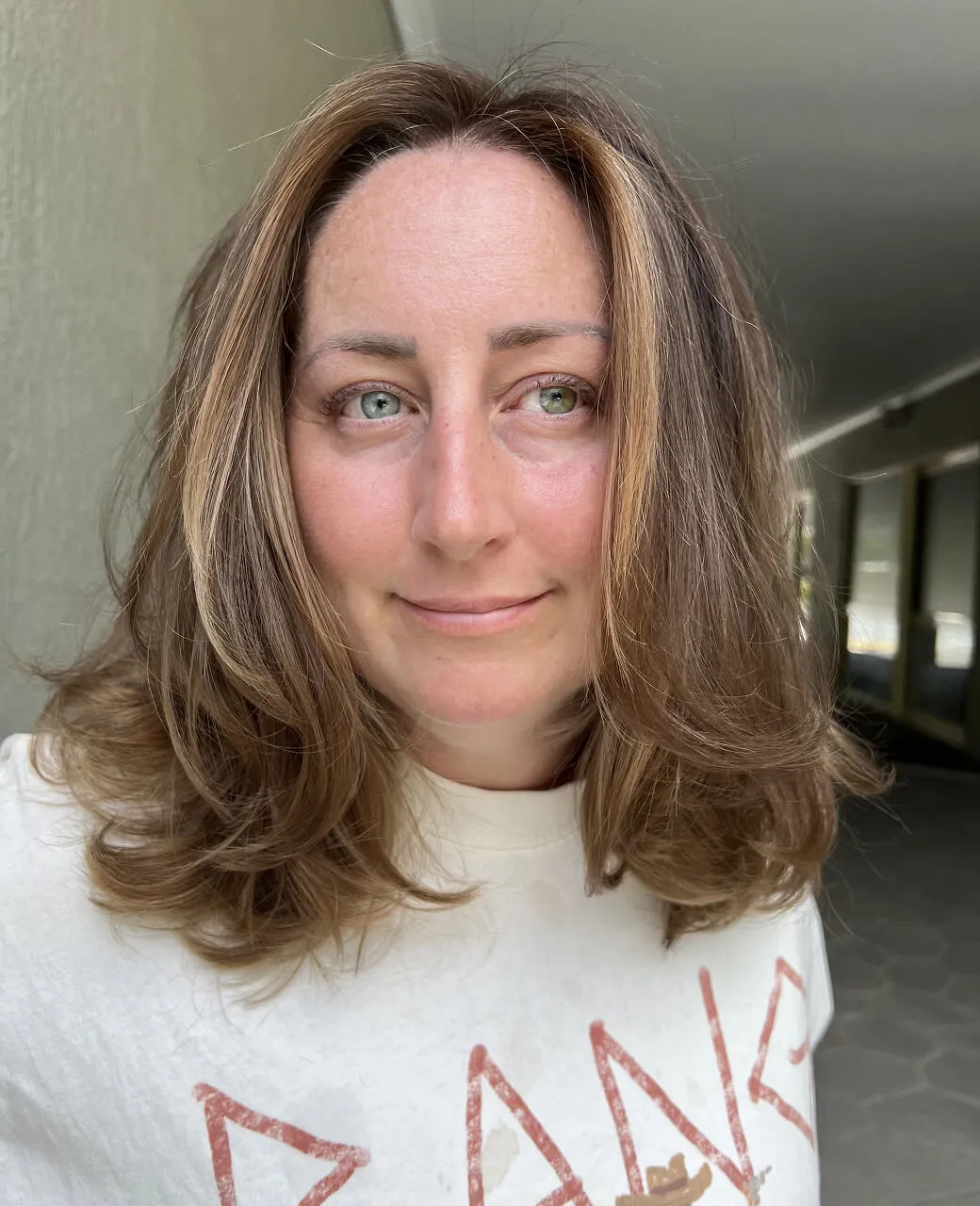 Woman with medium-length warm brunette hair and caramel tint highlights styled with soft waves at Jura Draco salon on the Gold Coast