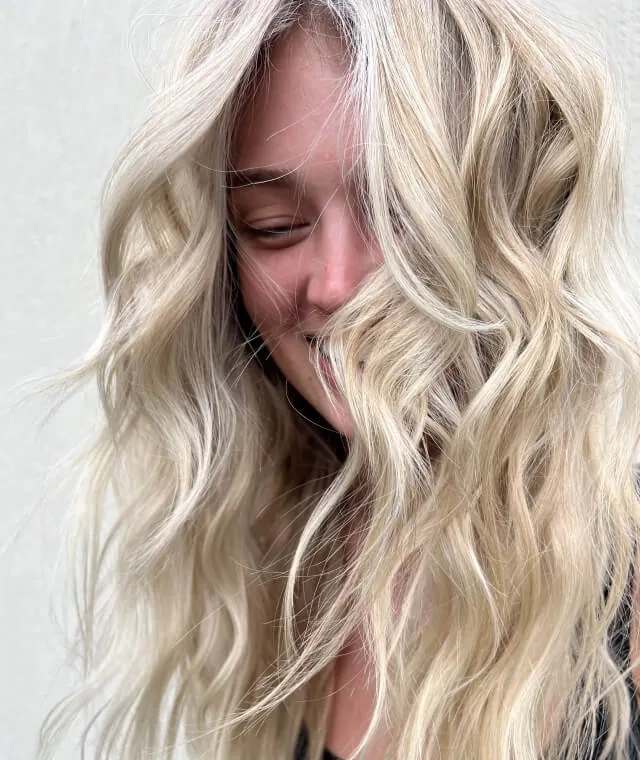 Close-up of a smiling woman with long, wavy blonde hair partially covering her face.