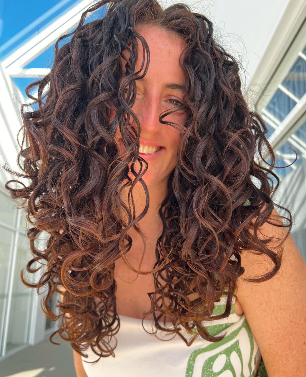 Woman with long defined brown curls after a curly haircut at Jura Draco Gold Coast