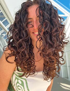Woman with long defined brown curls after a curly haircut at Jura Draco Gold Coast