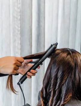 Long brown hair being styled into waves with a curling wand at Jura Draco Gold Coast