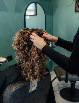 Stylist arranging a client's curly highlighted hair in the studio at Jura Draco Gold Coast