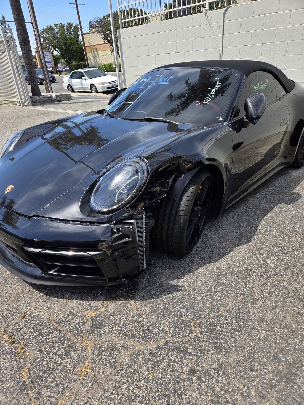 Black Porsche convertible with visible front-left damage parked near a concrete wall.